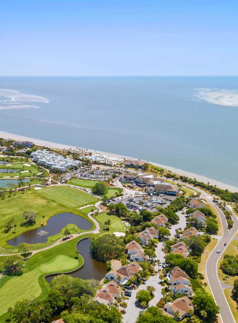 Aerial view of Seabrook Island coastline featuring oceanfront villas, lush green golf fairways, and the blue waters of the Atlantic Ocean.