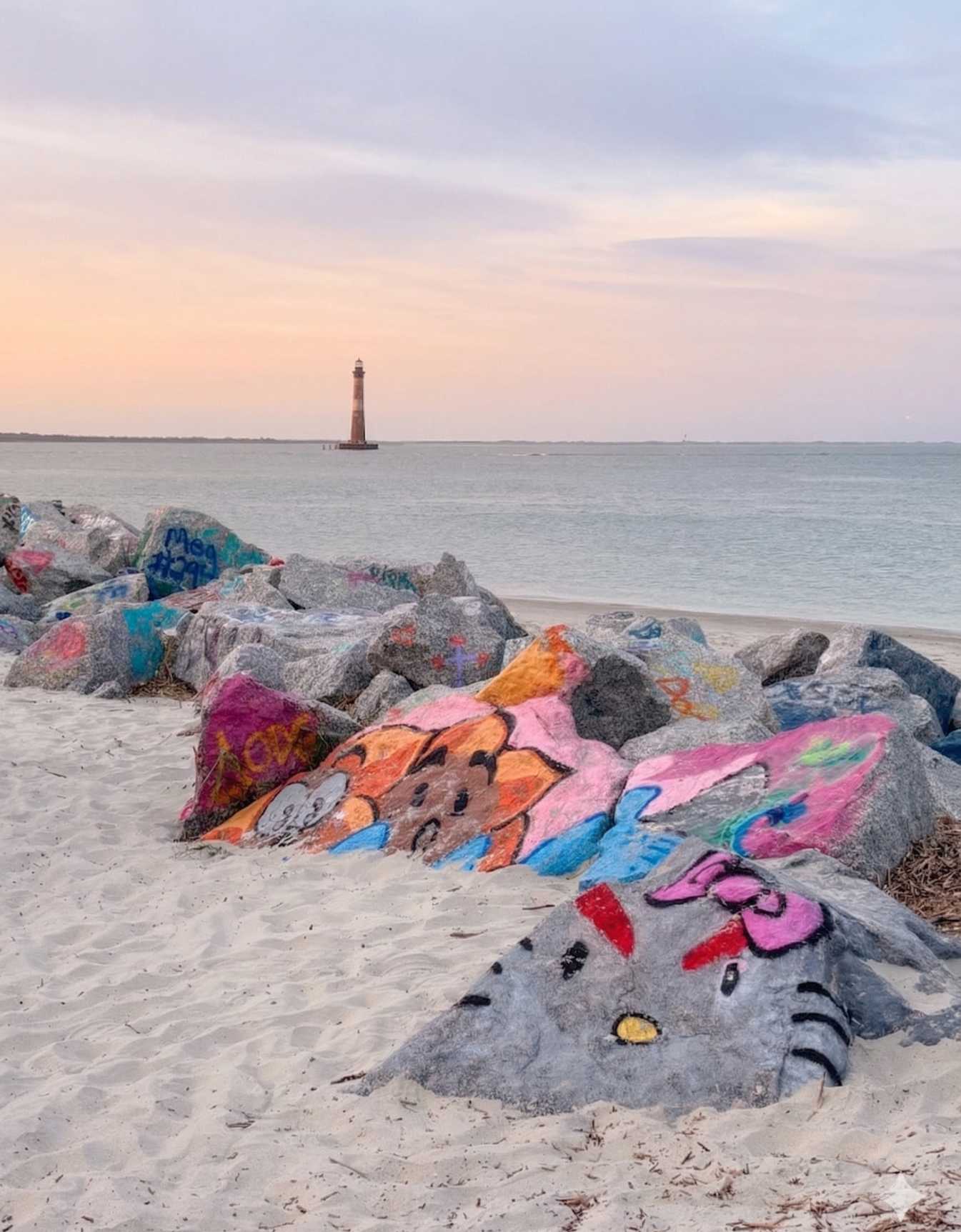 The historic Morris Island Lighthouse viewed from the beach with colorful painted rocks in the foreground at Folly Beach.